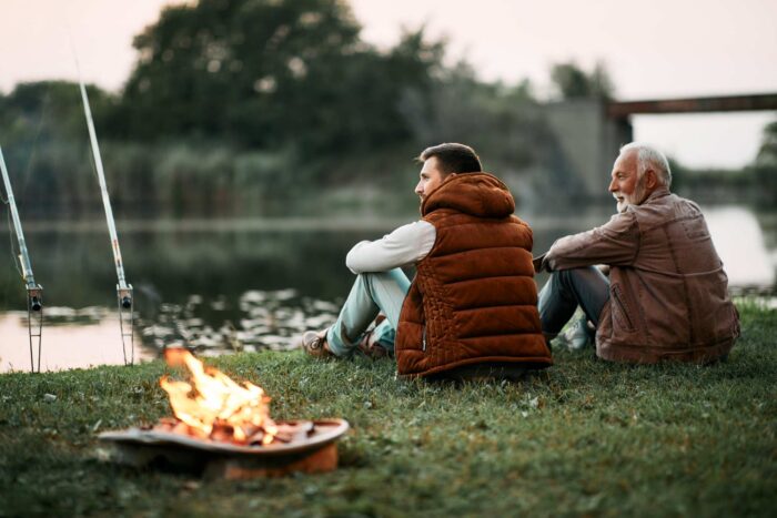 Two men sitting together and fishing by a river.
