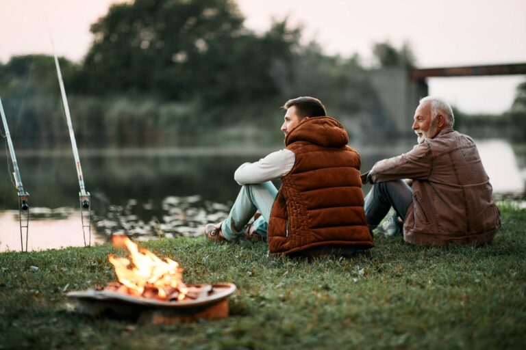 Two men sitting together and fishing by a river.
