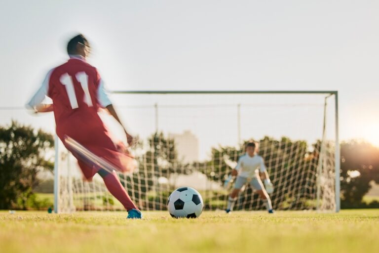 Soccer,,Goal,Post,And,Ball,,Soccer,Player,Running,And,Kicking A footballer taking a shot at a goal.