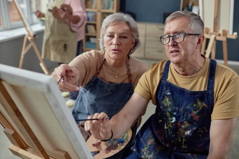 High,Angle,Portrait,Of,Senior,Couple,Painting,Picture,On,Easel An older couple painting at an easel together.